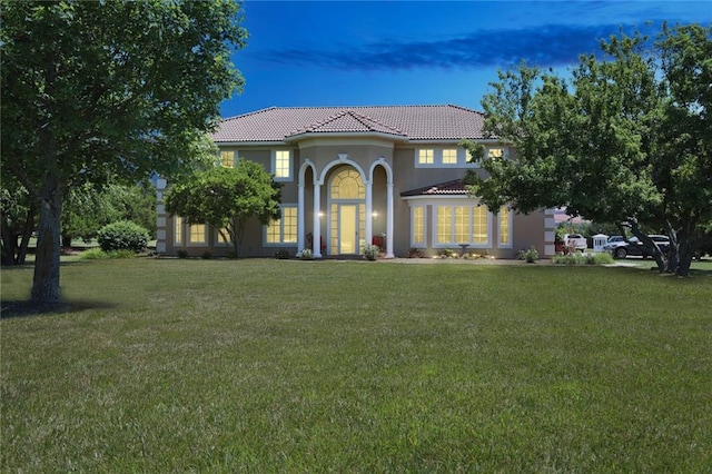 mediterranean / spanish-style home featuring a tiled roof, a front lawn, and stucco siding