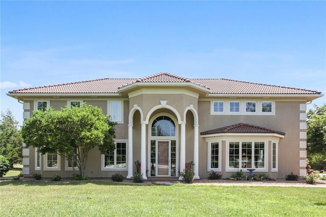 mediterranean / spanish home with a tile roof, a front lawn, and stucco siding