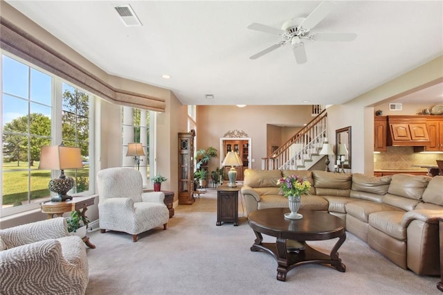 living room featuring light carpet, visible vents, stairway, and a ceiling fan