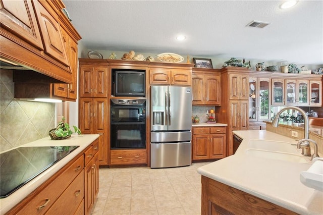 kitchen with brown cabinets, light countertops, visible vents, a sink, and black appliances