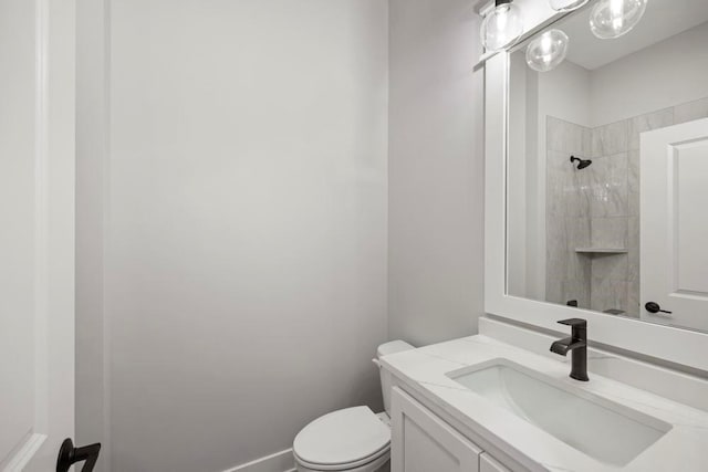 bathroom with a tile shower, vanity, and toilet