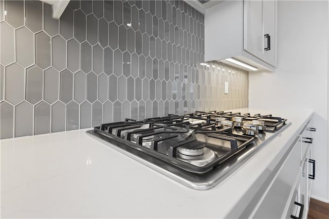 details featuring tasteful backsplash, white cabinets, and stainless steel gas cooktop