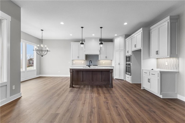 kitchen with sink, hanging light fixtures, an inviting chandelier, oven, and a kitchen island with sink