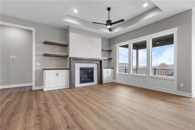 unfurnished living room featuring ceiling fan, light hardwood / wood-style floors, built in features, and a tray ceiling