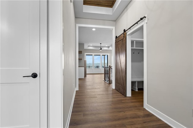 corridor featuring dark hardwood / wood-style floors, a barn door, and a tray ceiling