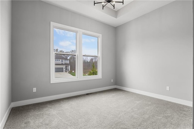 carpeted empty room with a tray ceiling and a notable chandelier