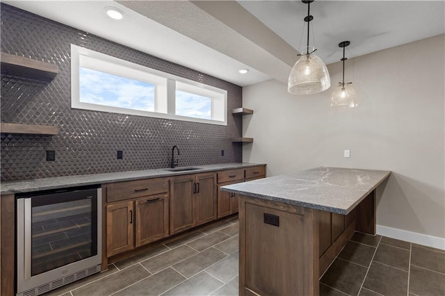 kitchen featuring tasteful backsplash, light stone counters, beverage cooler, sink, and hanging light fixtures