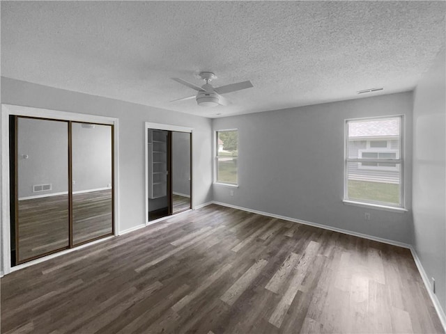 unfurnished bedroom with dark hardwood / wood-style floors, multiple closets, a textured ceiling, and ceiling fan