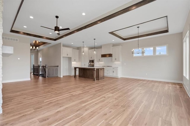 unfurnished living room featuring ceiling fan with notable chandelier, a raised ceiling, and light hardwood / wood-style floors