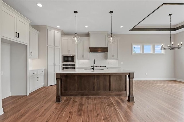 kitchen featuring wood-type flooring, hanging light fixtures, a kitchen island with sink, and a tray ceiling