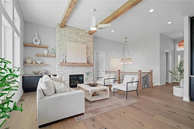 living room featuring a fireplace, ceiling fan with notable chandelier, vaulted ceiling with beams, and light hardwood / wood-style flooring