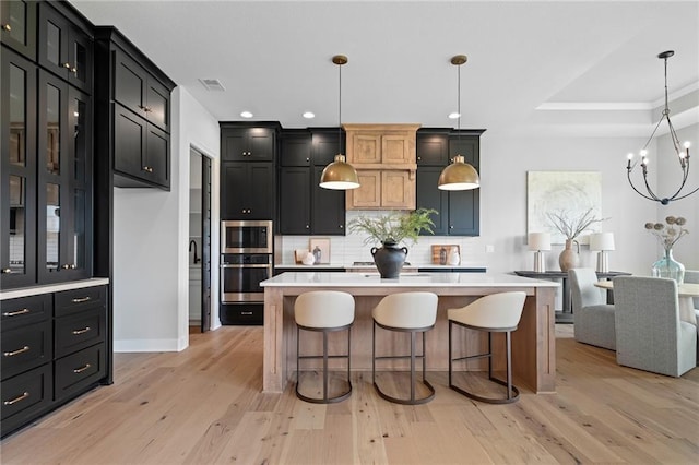 kitchen featuring a center island with sink, stainless steel appliances, decorative light fixtures, a kitchen bar, and decorative backsplash