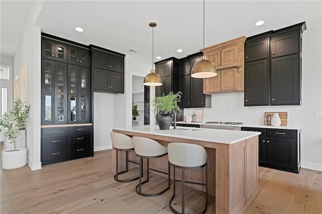 kitchen featuring light wood-type flooring, stainless steel gas cooktop, pendant lighting, sink, and a kitchen island with sink