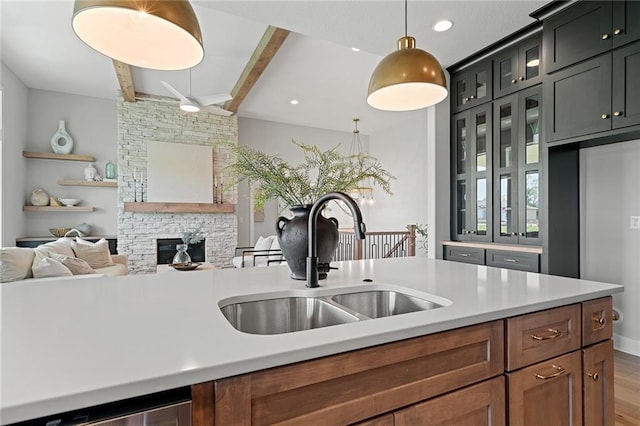 kitchen with a fireplace, hanging light fixtures, sink, wood-type flooring, and beamed ceiling