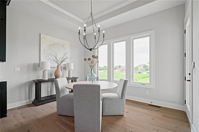 dining area featuring a notable chandelier, light hardwood / wood-style flooring, and a raised ceiling