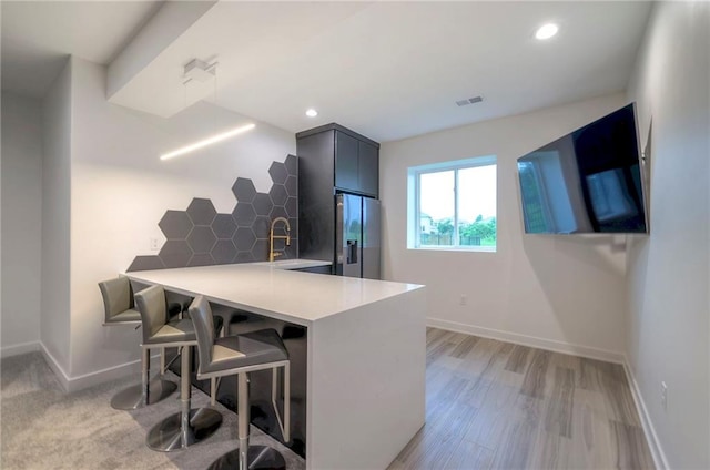 kitchen with stainless steel refrigerator with ice dispenser, sink, a kitchen breakfast bar, kitchen peninsula, and light hardwood / wood-style floors