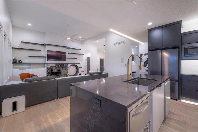 kitchen featuring sink, light hardwood / wood-style flooring, dark stone counters, an island with sink, and stainless steel appliances