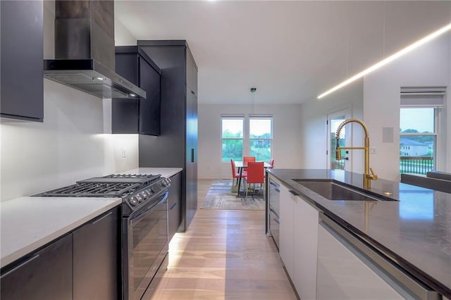 kitchen featuring pendant lighting, wall chimney range hood, sink, dishwasher, and range with gas cooktop