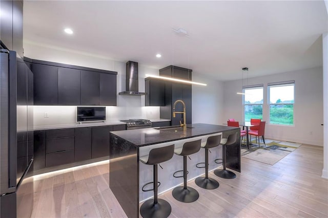 kitchen featuring pendant lighting, wall chimney range hood, sink, a kitchen island with sink, and stainless steel appliances