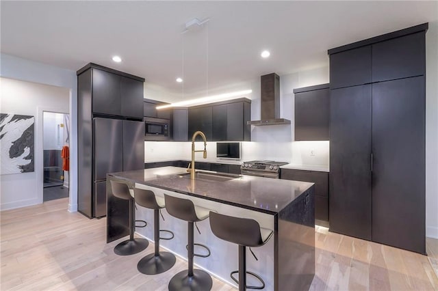 kitchen with sink, light hardwood / wood-style flooring, a center island with sink, built in microwave, and wall chimney exhaust hood