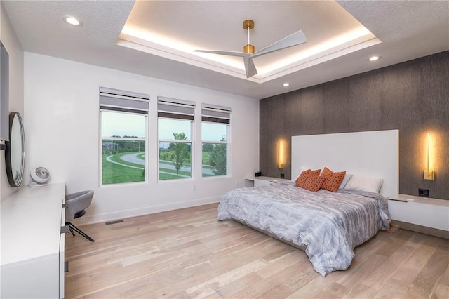 bedroom featuring a raised ceiling, ceiling fan, and light hardwood / wood-style flooring