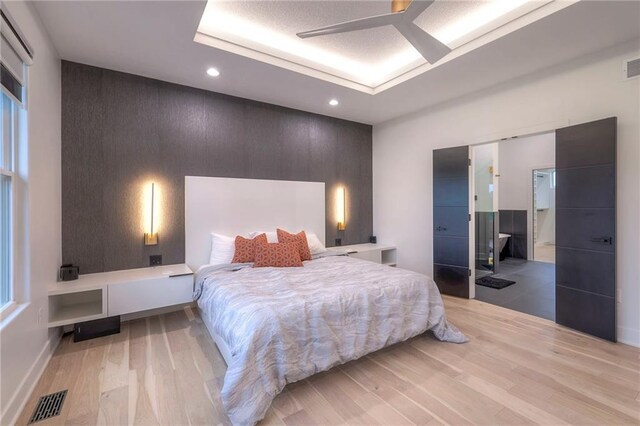 bedroom featuring ceiling fan, a raised ceiling, and light wood-type flooring