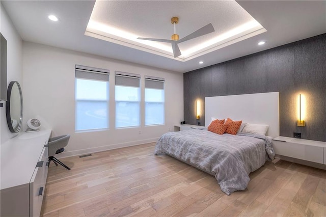 bedroom with light hardwood / wood-style flooring, a raised ceiling, and ceiling fan