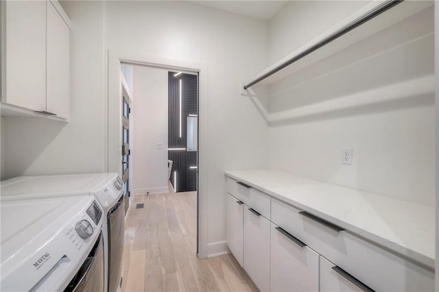 laundry room featuring cabinets, light wood-type flooring, and washer and clothes dryer