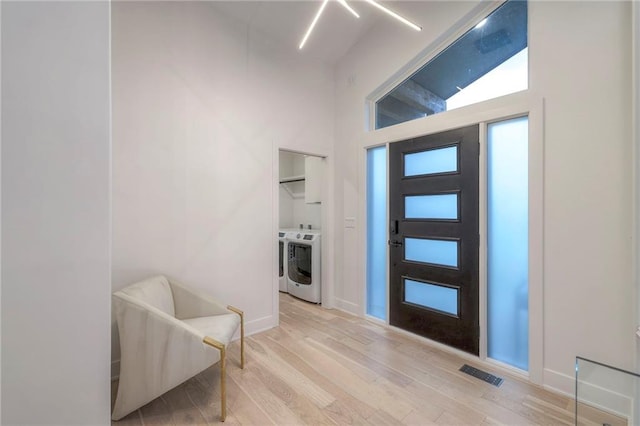 foyer entrance featuring a towering ceiling, washer and clothes dryer, and light hardwood / wood-style flooring