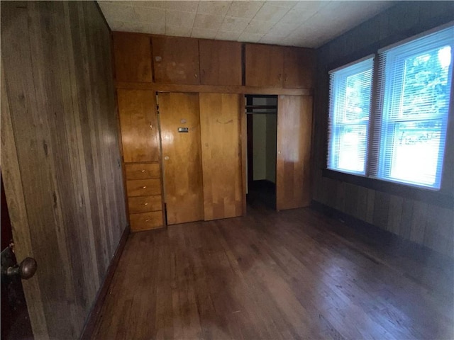 unfurnished bedroom featuring dark wood-type flooring, wood walls, multiple windows, and a closet