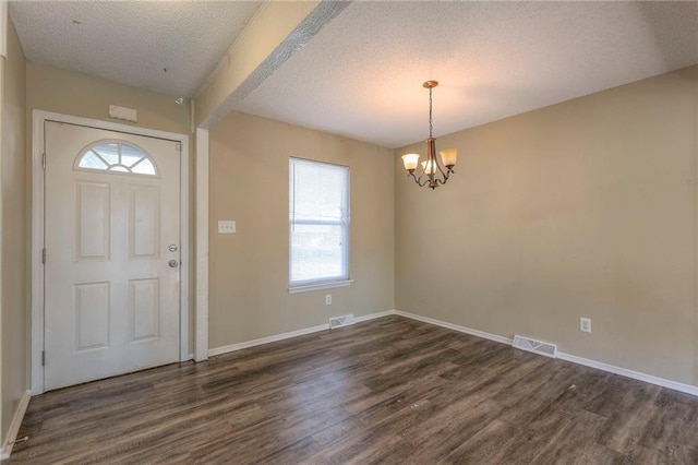 foyer entrance with dark hardwood / wood-style flooring, an inviting chandelier, a textured ceiling, and a wealth of natural light