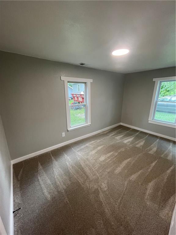 spare room featuring dark carpet and a wealth of natural light