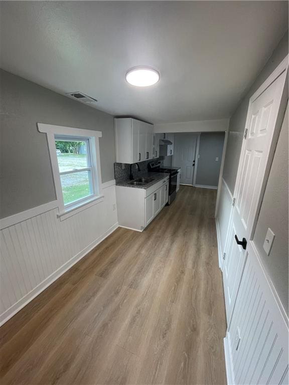 kitchen featuring white cabinetry, stainless steel stove, backsplash, hardwood / wood-style floors, and sink