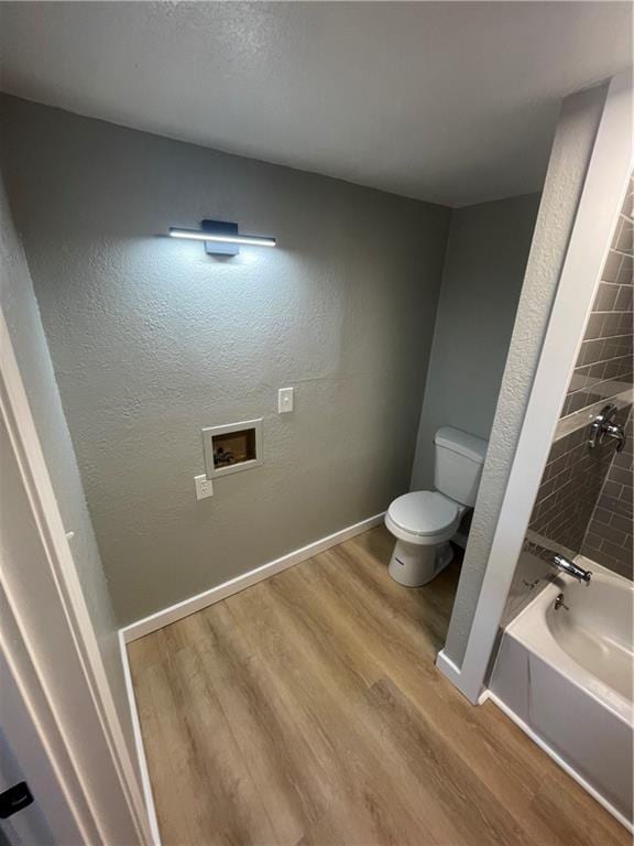 bathroom with a tub to relax in, wood-type flooring, and toilet