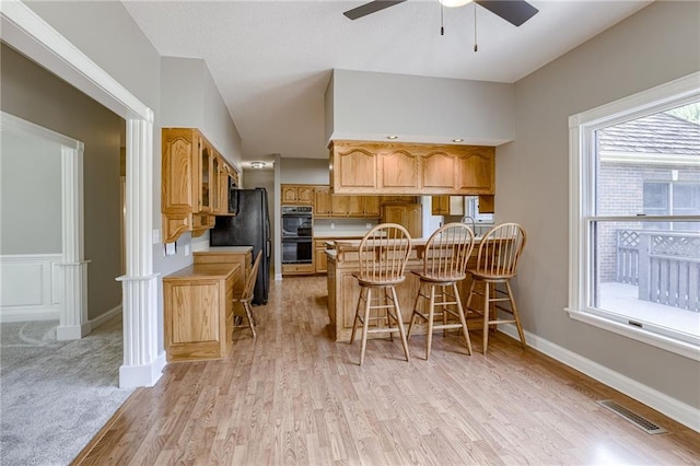 kitchen featuring kitchen peninsula, light wood-type flooring, a breakfast bar, ceiling fan, and black appliances