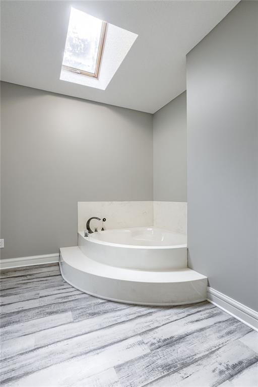 bathroom with hardwood / wood-style flooring, a washtub, and a skylight