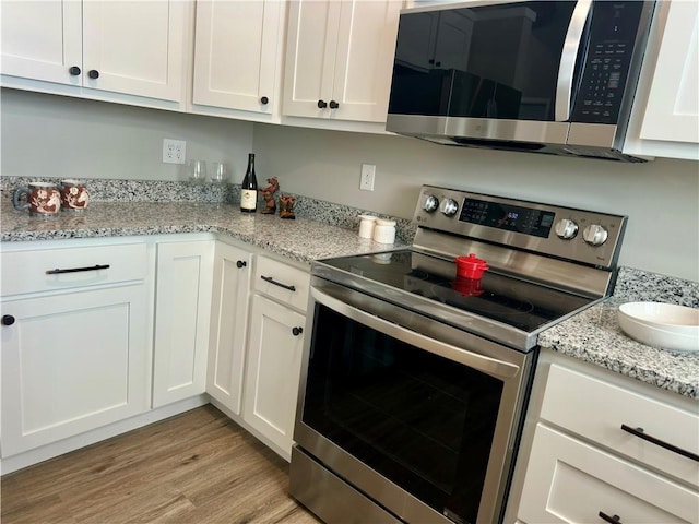 kitchen featuring light stone countertops, appliances with stainless steel finishes, white cabinets, and light wood-type flooring