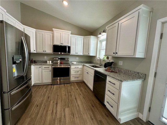 kitchen featuring sink, dark wood-type flooring, appliances with stainless steel finishes, white cabinetry, and vaulted ceiling