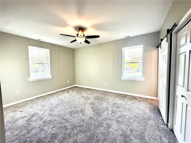 empty room featuring a barn door, a healthy amount of sunlight, carpet, and ceiling fan