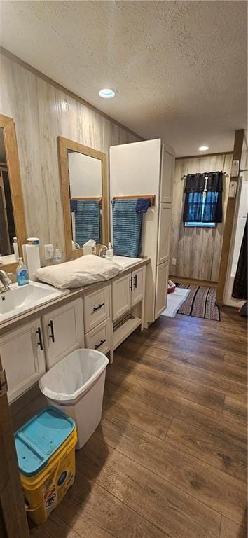 bathroom featuring vanity, hardwood / wood-style floors, a textured ceiling, and wooden walls