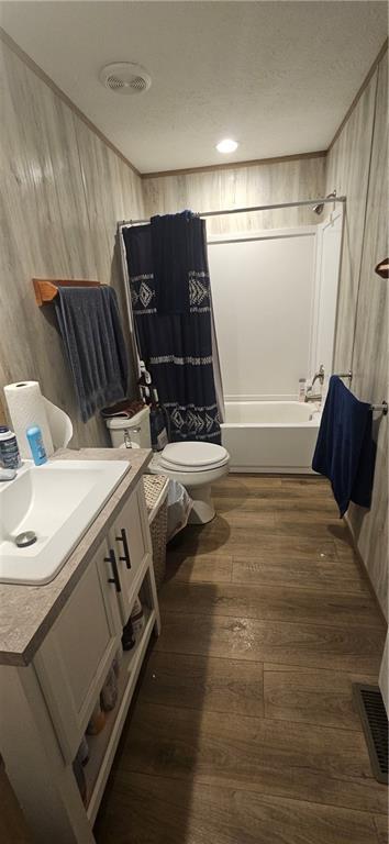 full bathroom with shower / bath combo, vanity, wooden walls, toilet, and wood-type flooring