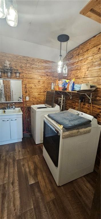 clothes washing area with washing machine and clothes dryer, dark hardwood / wood-style flooring, wooden walls, and sink