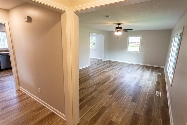 empty room with baseboards, visible vents, ceiling fan, dark wood-type flooring, and a textured ceiling