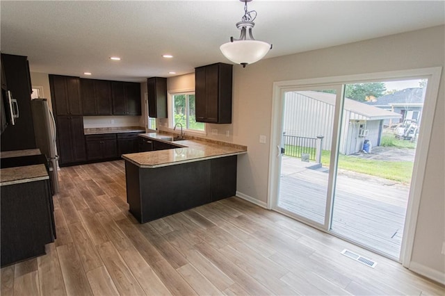 kitchen with recessed lighting, a peninsula, visible vents, light wood-style floors, and dark brown cabinets