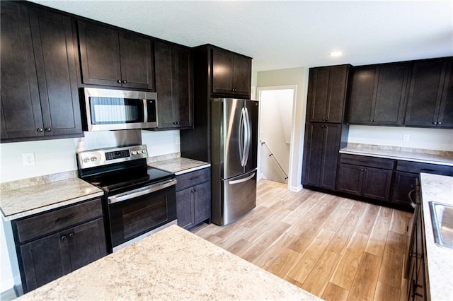 kitchen featuring baseboards, appliances with stainless steel finishes, light countertops, light wood-style floors, and a sink