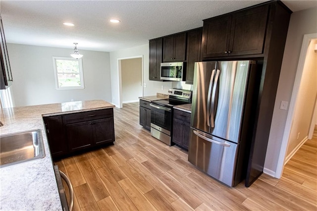 kitchen with appliances with stainless steel finishes, a sink, a textured ceiling, and light wood finished floors