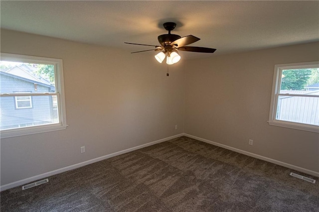 empty room with a ceiling fan, visible vents, dark carpet, and baseboards