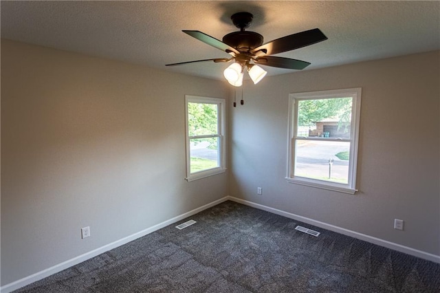 spare room featuring dark carpet, visible vents, plenty of natural light, and baseboards