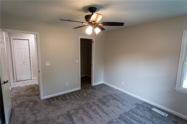 unfurnished bedroom featuring baseboards, visible vents, a textured ceiling, dark carpet, and a closet