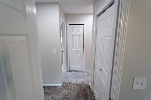 hallway with baseboards and dark colored carpet